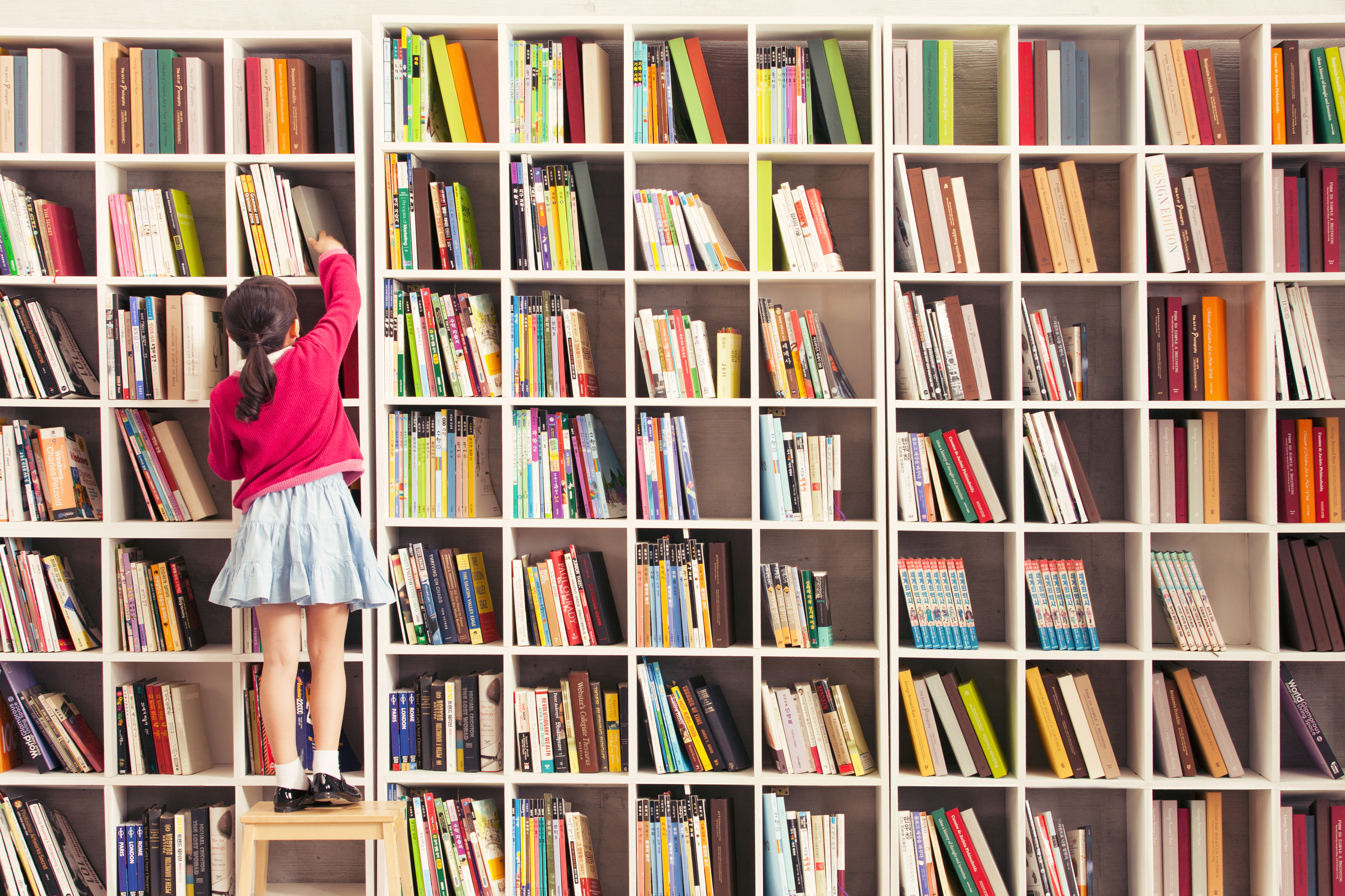 Child reaching for books on colorful bookshelves — the joy of learning and growing